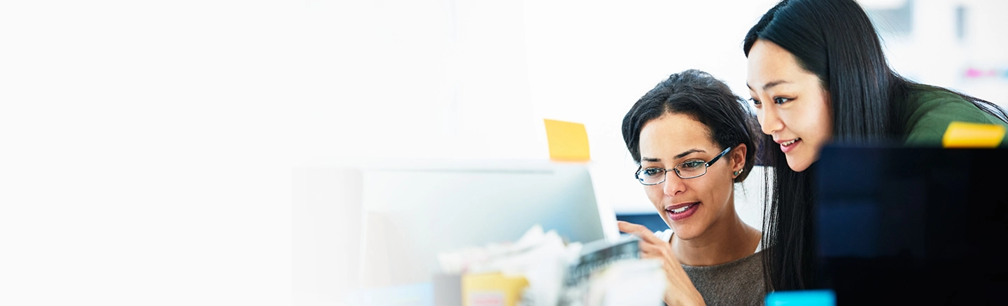 Two professionals collaborating at a computer in a modern office environment with colorful sticky notes