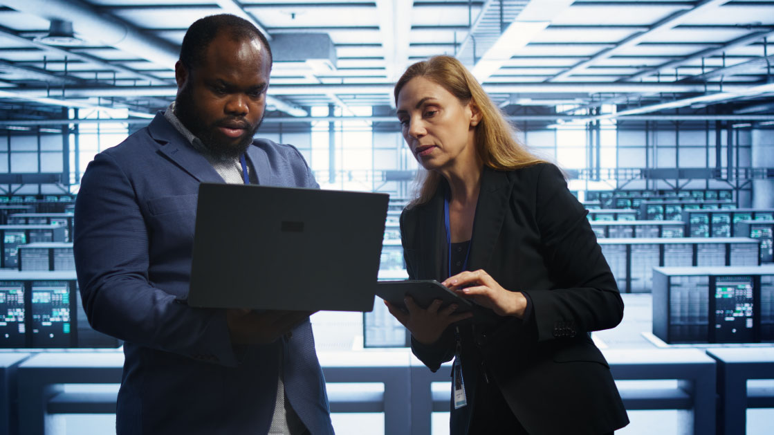 Un homme et une femme regardent un ordinateur portable dans une salle de serveurs.